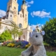 Ein Plüsch-Nashorn sitzt vor einem Blumenbeet, im Hintergrund ist der Dom von Brixen vor blauem Himmel zu sehen.